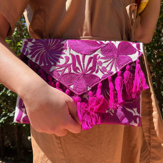 Bohemian pink floral embroidered clutch bag with tassels held by a person wearing a brown dress outdoors
