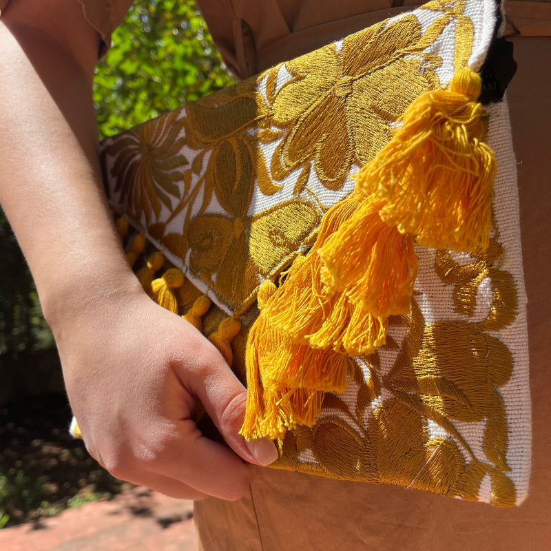 Mustard yellow floral embroidered clutch bag with tassels held by a person wearing a brown dress outdoors
