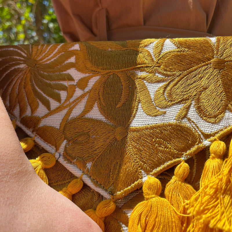 Mustard yellow floral embroidered clutch bag with tassels held by a person wearing a brown dress outdoors