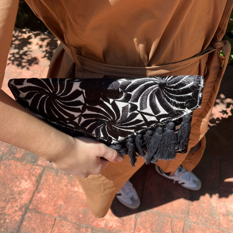 Woman holding a black and white embroidered clutch with tassels in a monochrome boho style outdoors