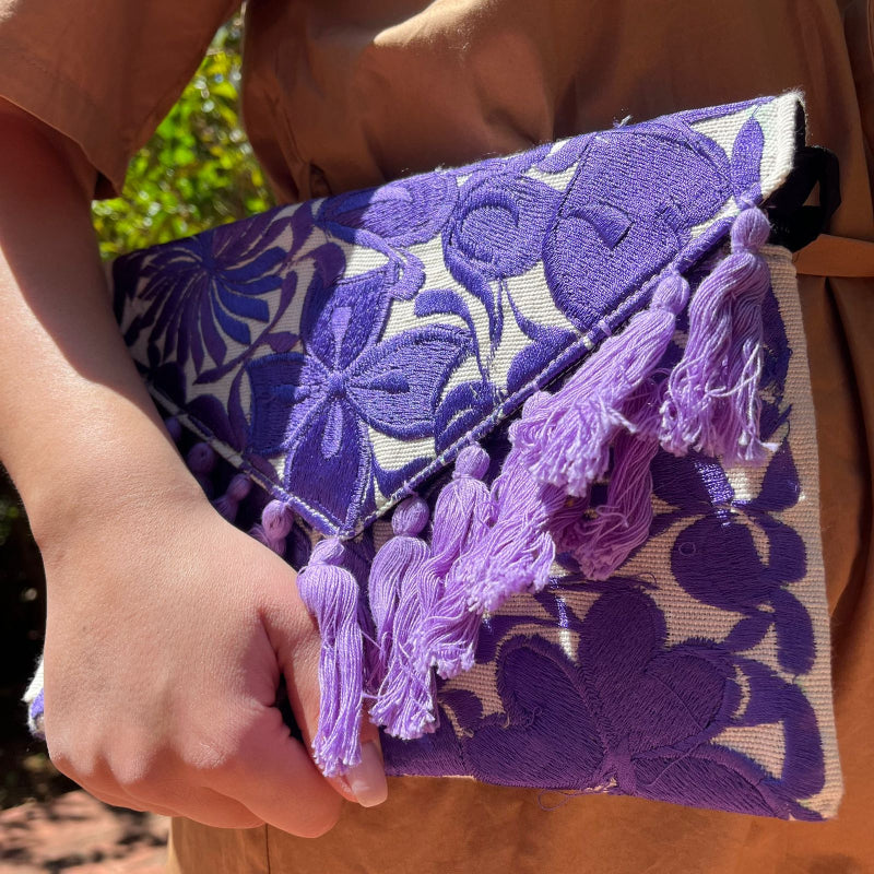 Purple floral embroidered clutch bag with tassels held by a person wearing a brown dress outdoors