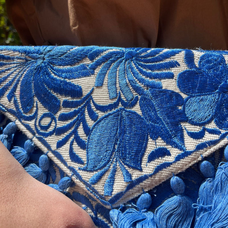 Blue floral embroidered clutch bag with tassels held by a person wearing a brown dress outdoors