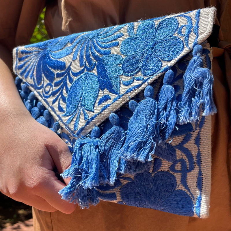 Blue floral embroidered clutch bag with tassels held by a person wearing a brown dress outdoors