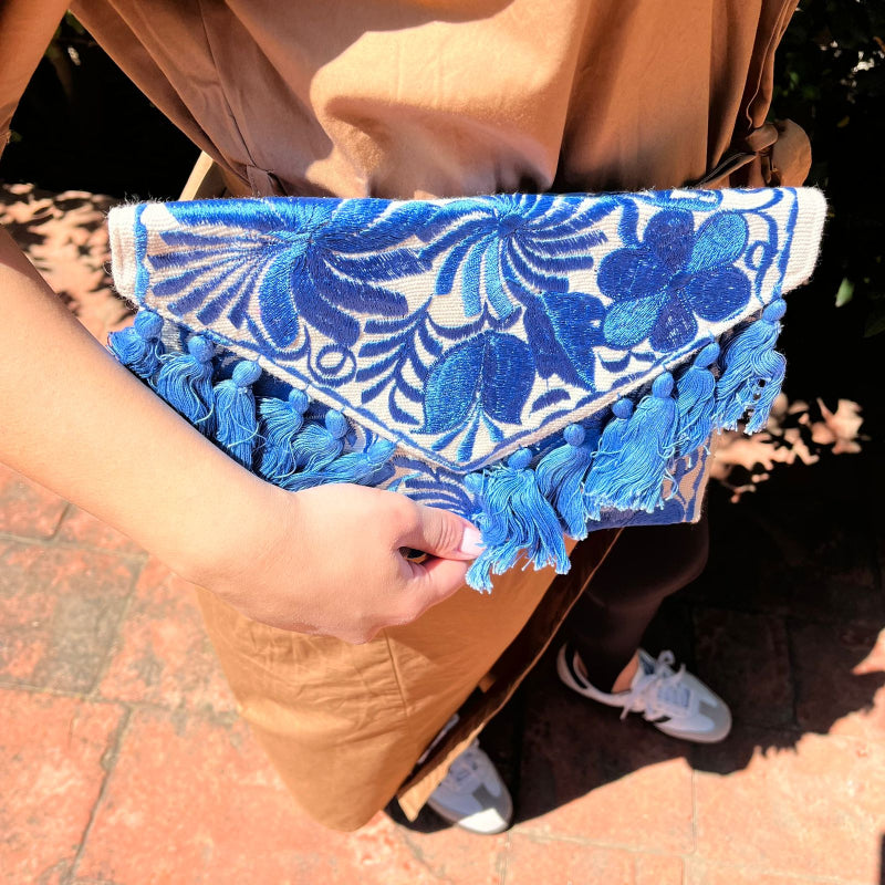 Blue floral embroidered clutch bag with tassels held by a person wearing a brown dress outdoors