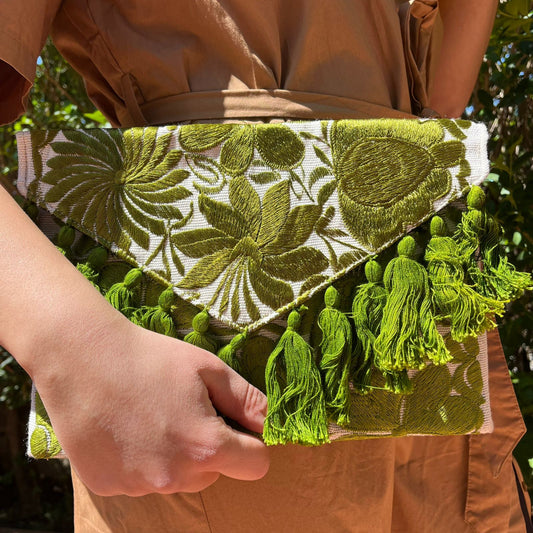 Olive green floral embroidered clutch bag with tassels held by a person wearing a brown dress outdoors