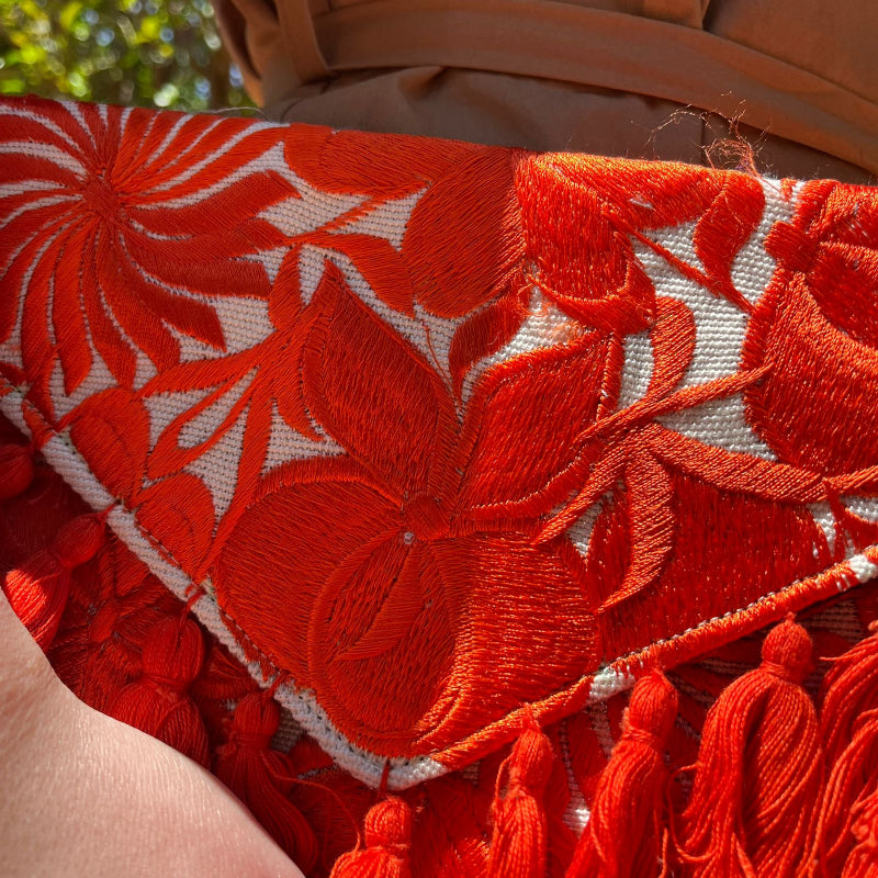 Red floral embroidered clutch bag with tassels held by a person wearing a brown dress outdoors