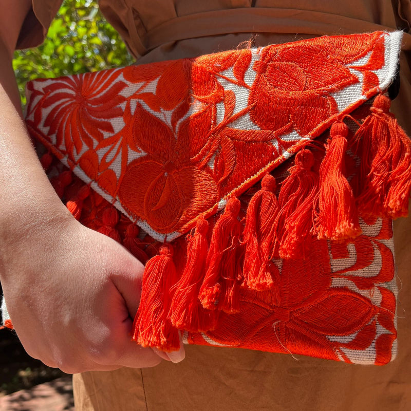 Red floral embroidered clutch bag with tassels held by a person wearing a brown dress outdoors