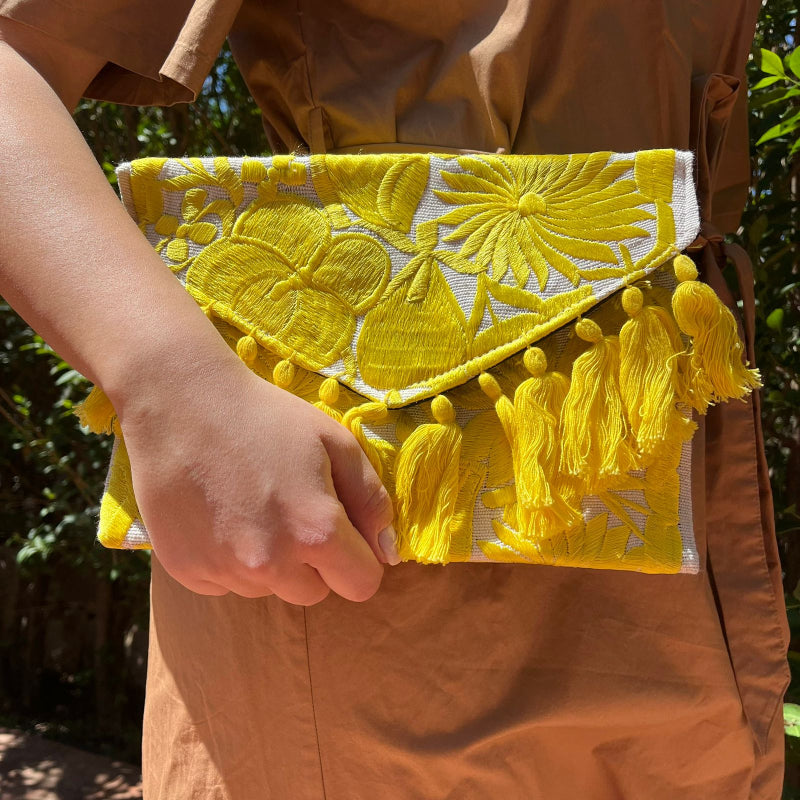 Bright yellow floral embroidered clutch bag with tassels held by a person wearing a brown dress outdoors