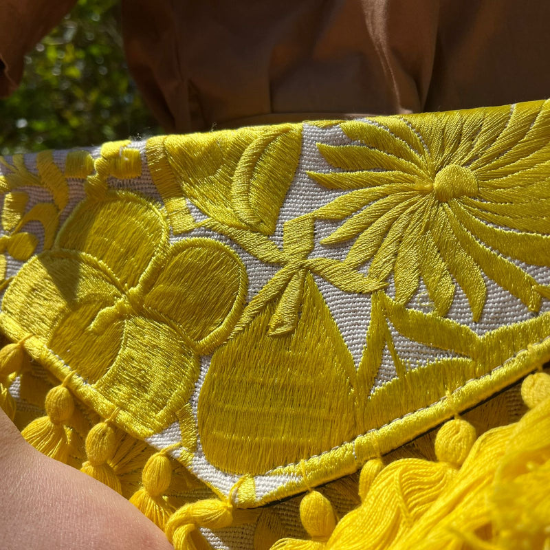 Bright yellow floral embroidered clutch bag with tassels held by a person wearing a brown dress outdoors