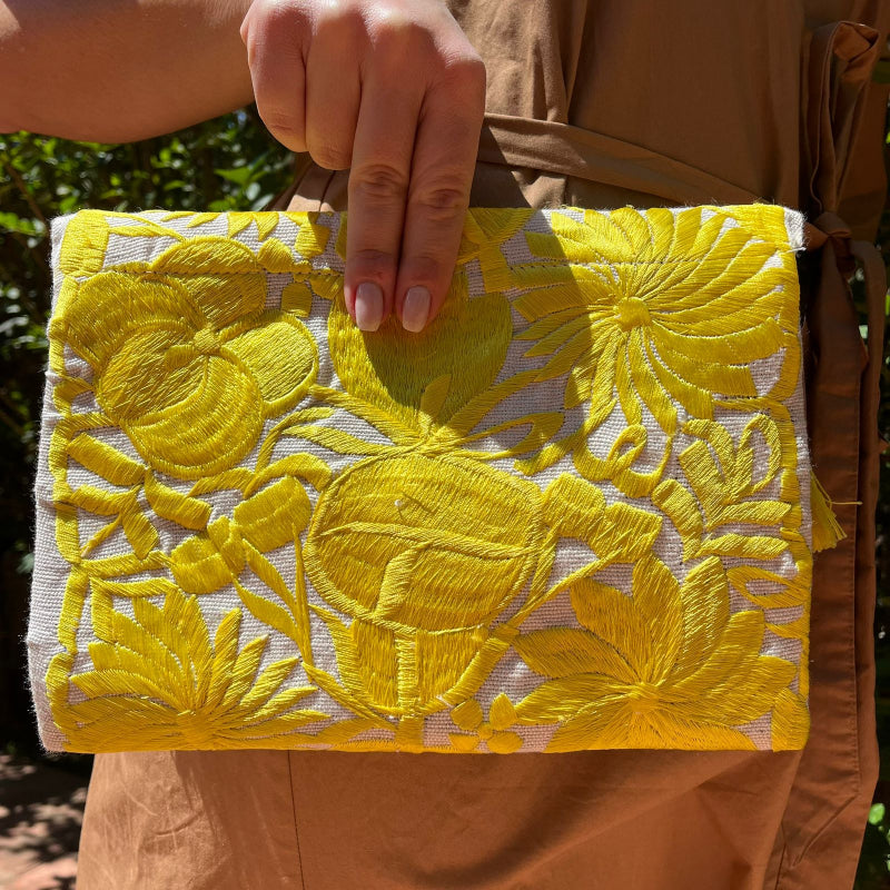 Bright yellow floral embroidered clutch bag with tassels held by a person wearing a brown dress outdoors