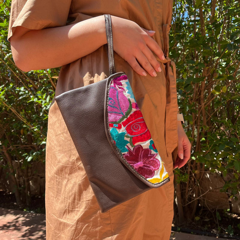 Woman wearing a brown leather shoulder bag with colorful floral embroidered flap outdoors