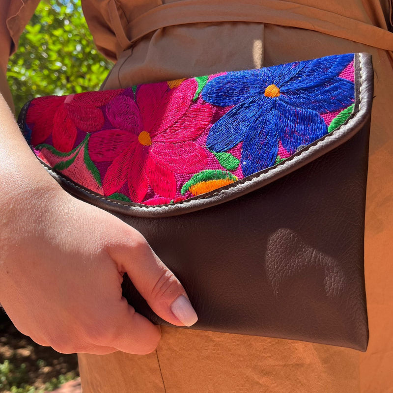 Woman wearing a brown leather shoulder bag with bold red floral embroidered flap outdoors