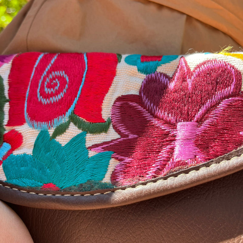 Woman wearing a brown leather shoulder bag with colorful floral embroidered flap outdoors