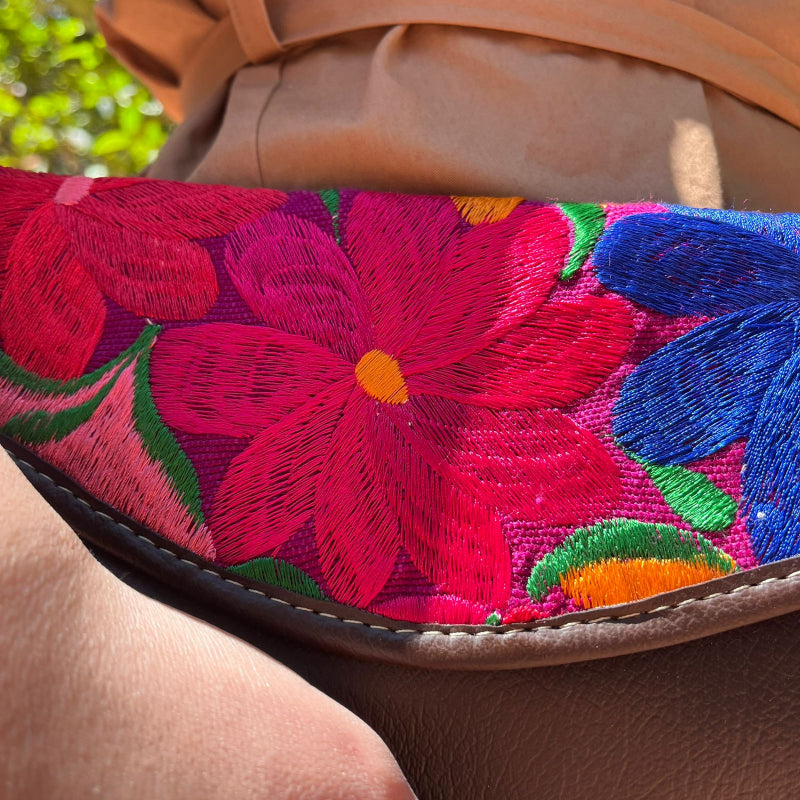 Woman wearing a brown leather shoulder bag with bold red floral embroidered flap outdoors