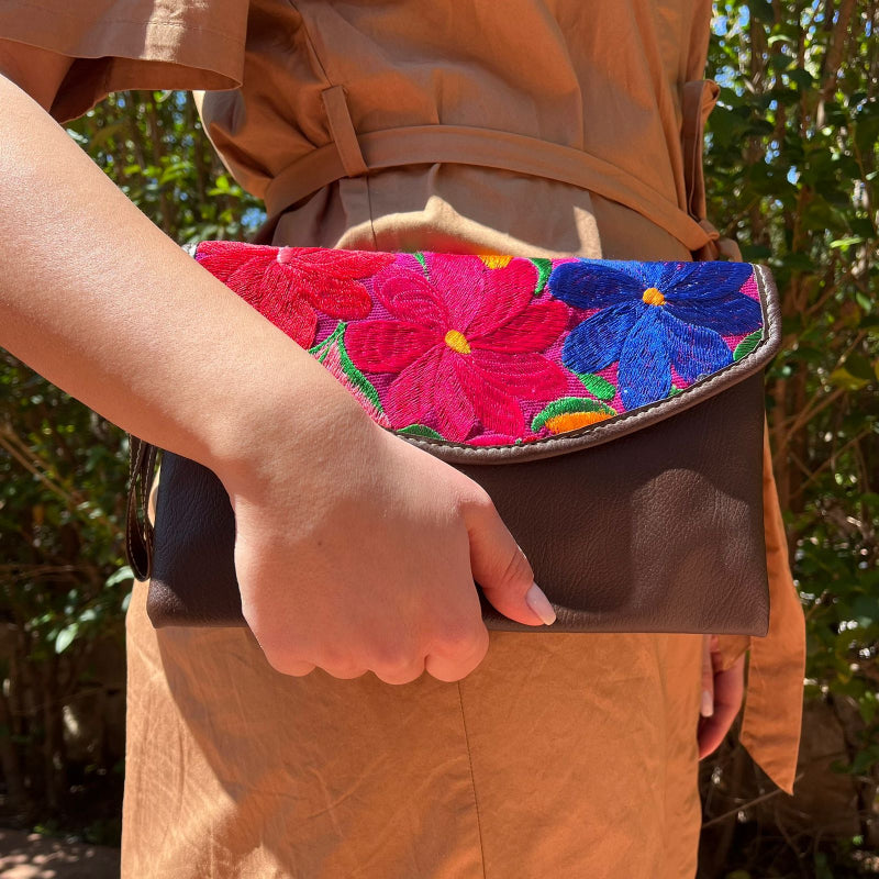 Woman wearing a brown leather shoulder bag with bold red floral embroidered flap outdoors