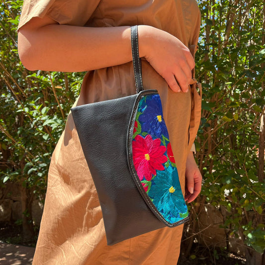 Woman wearing a black leather shoulder bag with colorful floral embroidered flap outdoors
