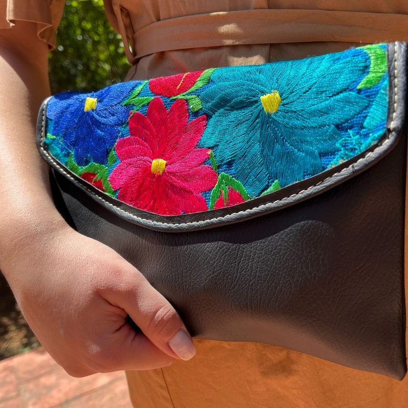 Woman wearing a black leather shoulder bag with colorful floral embroidered flap outdoors