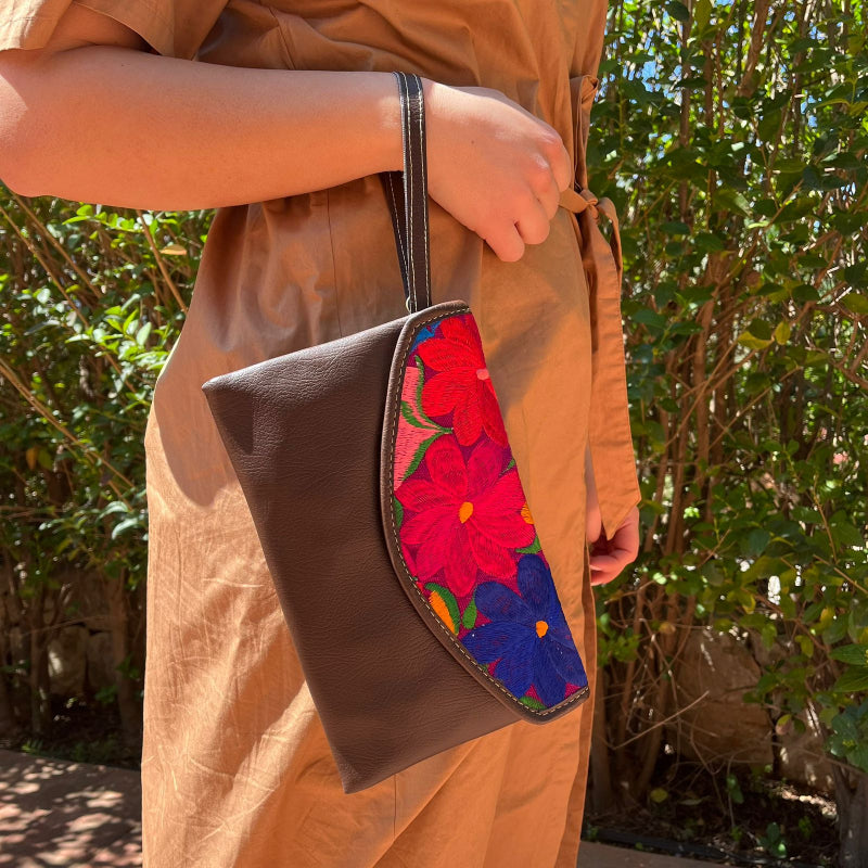 Woman wearing a brown leather shoulder bag with bold red floral embroidered flap outdoors