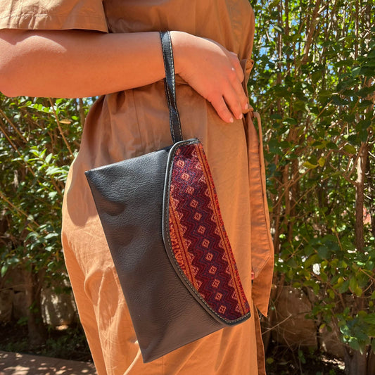 Woman wearing a black leather shoulder bag with tribal embroidered flap in earthy tones outdoors