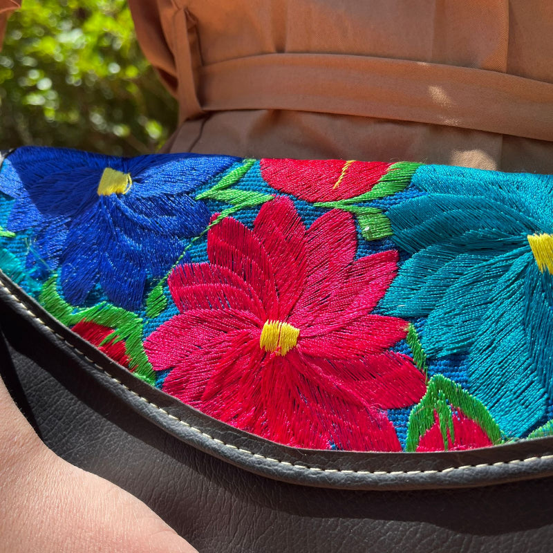 Woman wearing a black leather shoulder bag with colorful floral embroidered flap outdoors