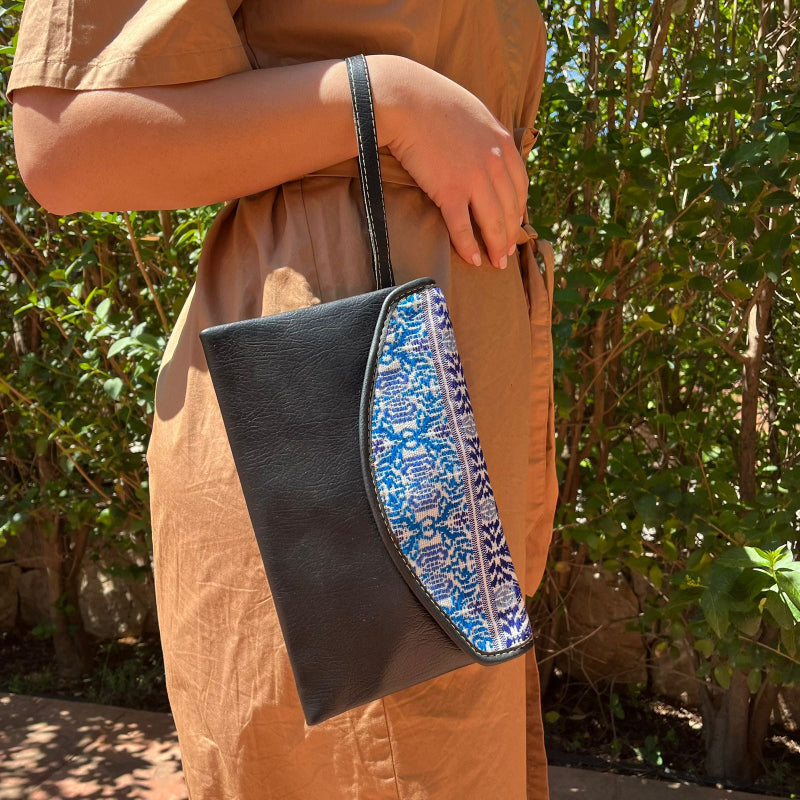 Woman wearing a black leather shoulder bag with blue patterned embroidered flap outdoors