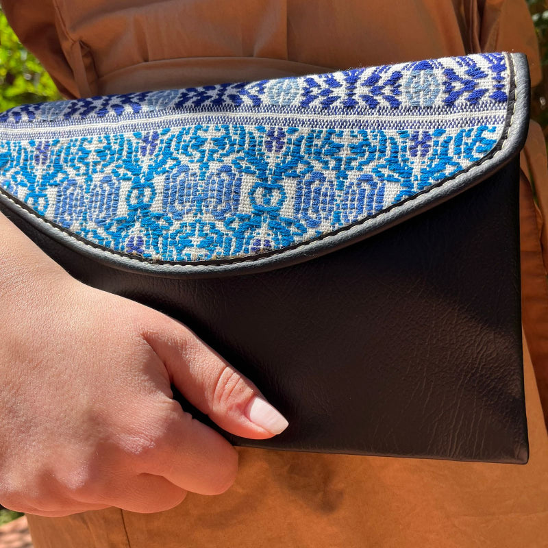 Woman wearing a black leather shoulder bag with blue patterned embroidered flap outdoors