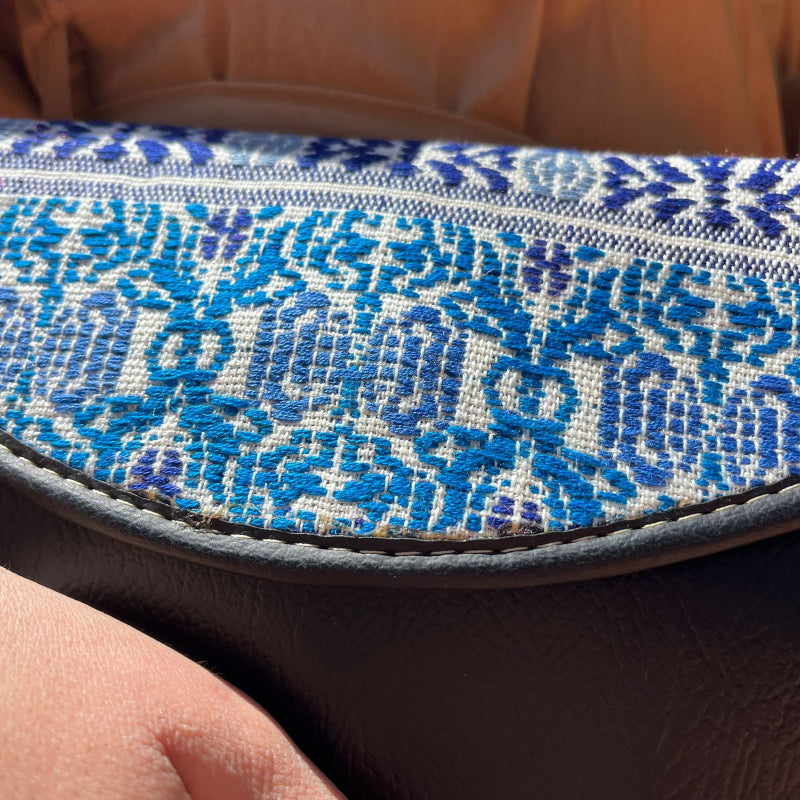 Woman wearing a black leather shoulder bag with blue patterned embroidered flap outdoors