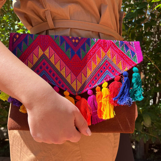 Woman holding a colorful tribal embroidered clutch with multicolor tassels and suede leather base outdoors