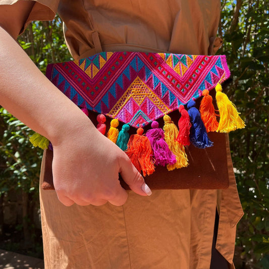 Woman holding a colorful tribal embroidered clutch with multicolor tassels and suede leather base outdoors