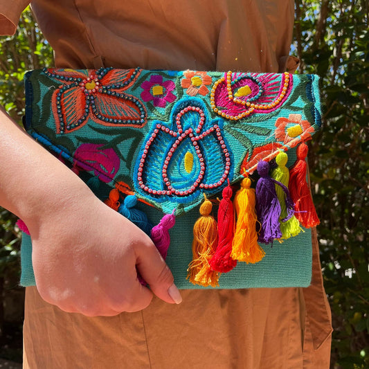 Woman holding a colorful floral embroidered clutch with bead details and multicolor tassels on a turquoise base outdoors