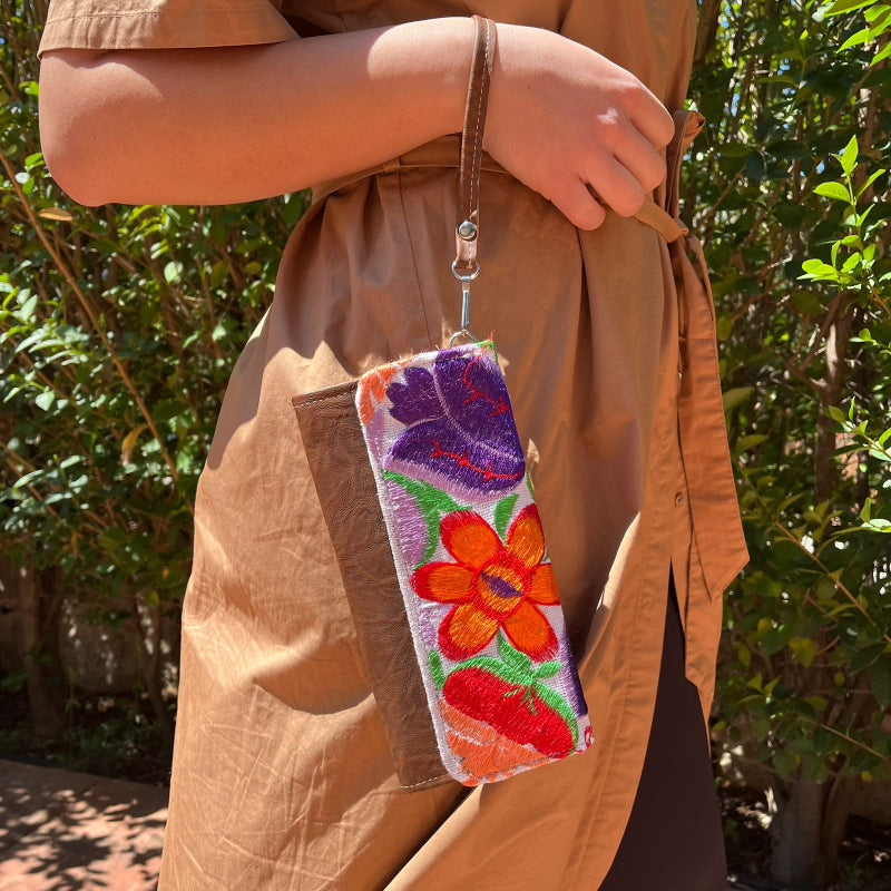 Woman holding a handmade leather clutch with vibrant colorful floral embroidery and wrist strap outdoors