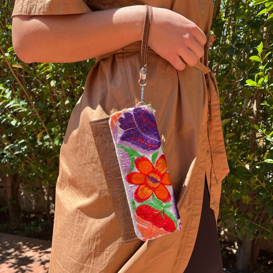 Woman holding a handmade leather clutch with vibrant colorful floral embroidery and wrist strap outdoors