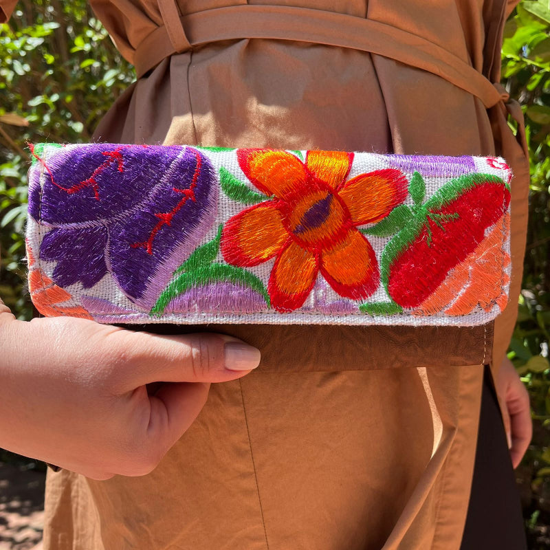 Woman holding a handmade leather clutch with vibrant colorful floral embroidery and wrist strap outdoors