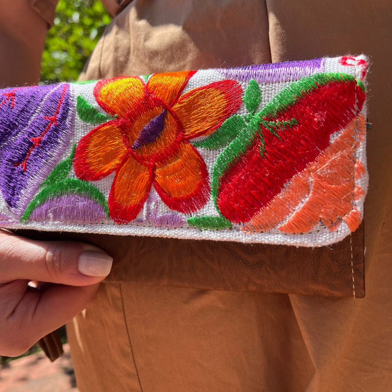 Woman holding a handmade leather clutch with vibrant colorful floral embroidery and wrist strap outdoors
