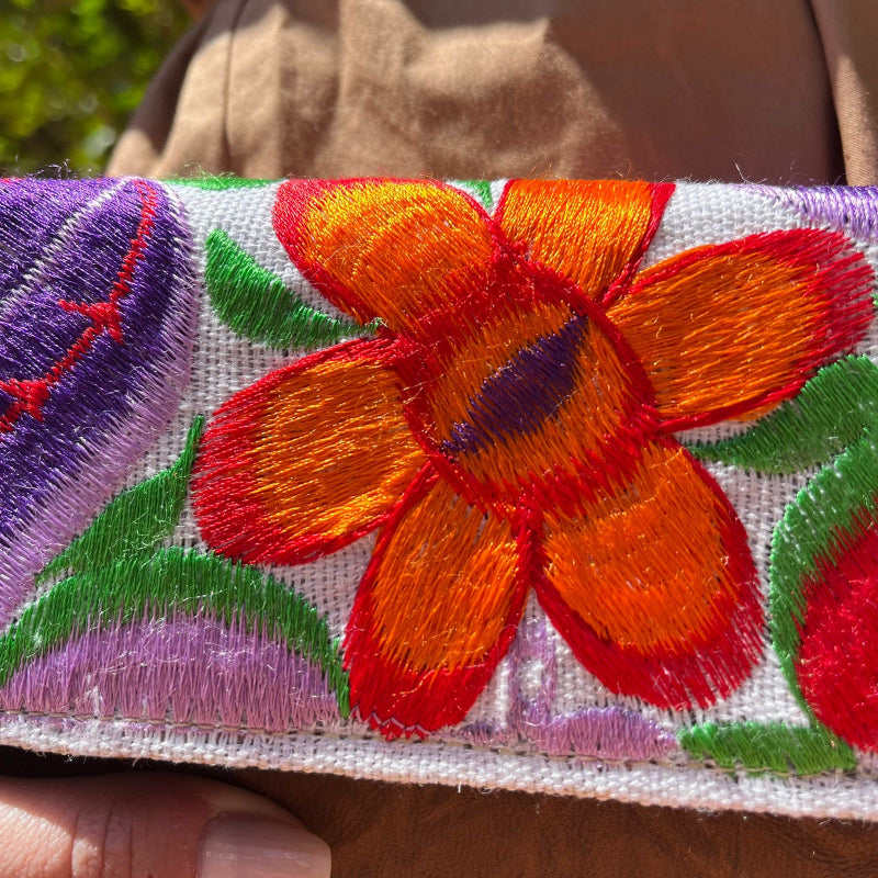Woman holding a handmade leather clutch with vibrant colorful floral embroidery and wrist strap outdoors