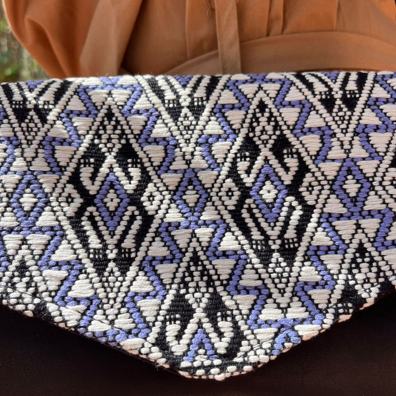 Handcrafted black leather crossbody bag with geometric woven flap worn outdoors