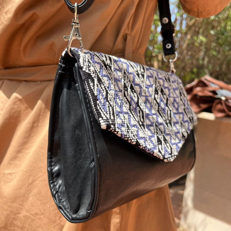 Handcrafted black leather crossbody bag with geometric woven flap worn outdoors