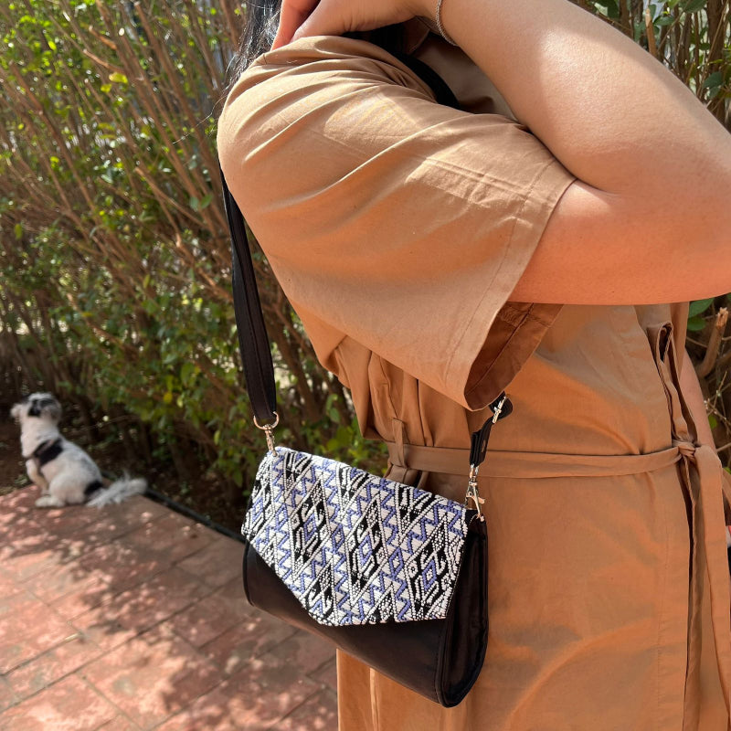 Handcrafted black leather crossbody bag with geometric woven flap worn outdoors