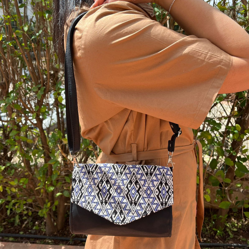 Handcrafted black leather crossbody bag with geometric woven flap worn outdoors
