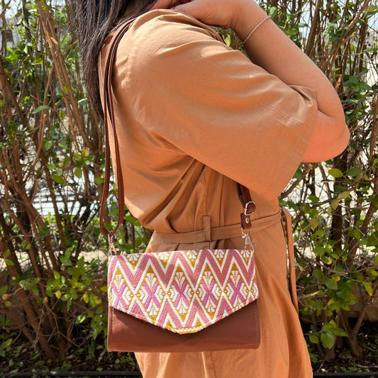 Woman wearing a brown leather crossbody bag with pink and gold geometric woven flap outdoors
