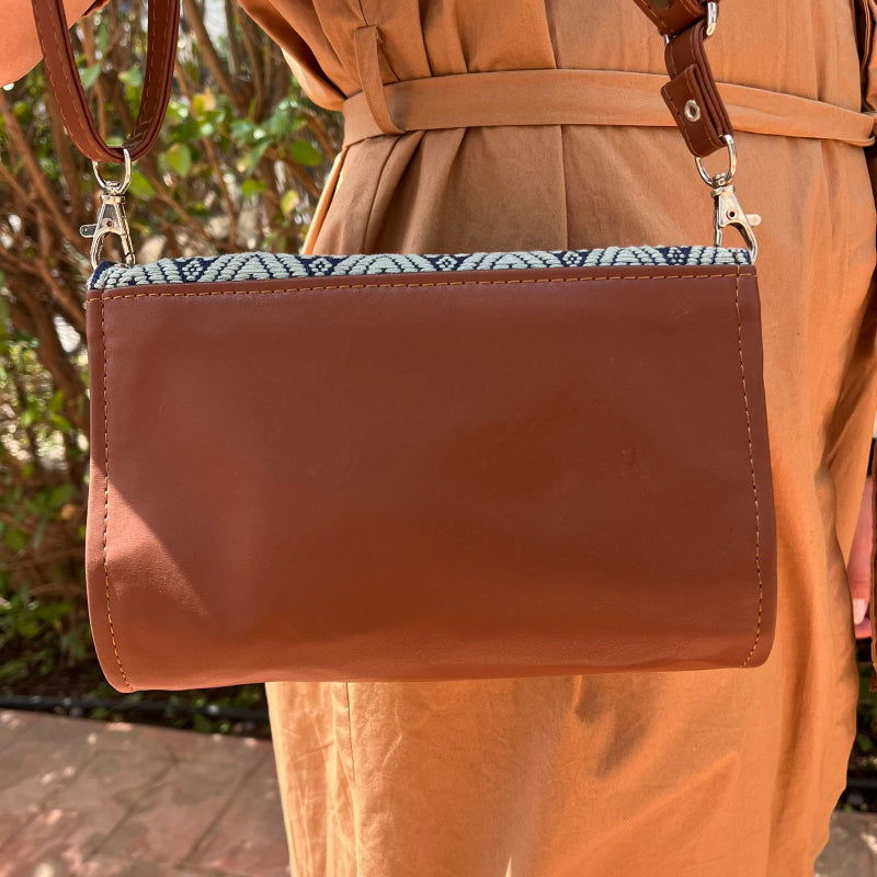 Woman wearing a brown leather crossbody bag with black and grey geometric woven flap outdoors