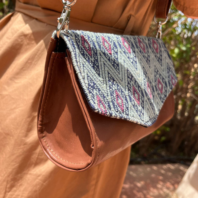 Woman wearing a brown leather crossbody bag with black and grey geometric woven flap outdoors