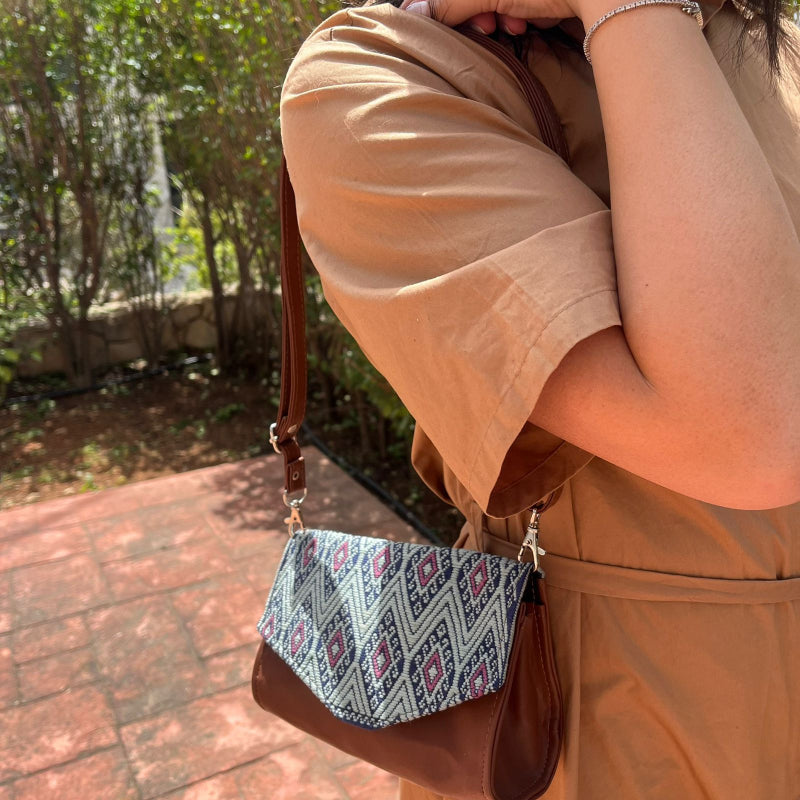 Woman wearing a brown leather crossbody bag with black and grey geometric woven flap outdoors