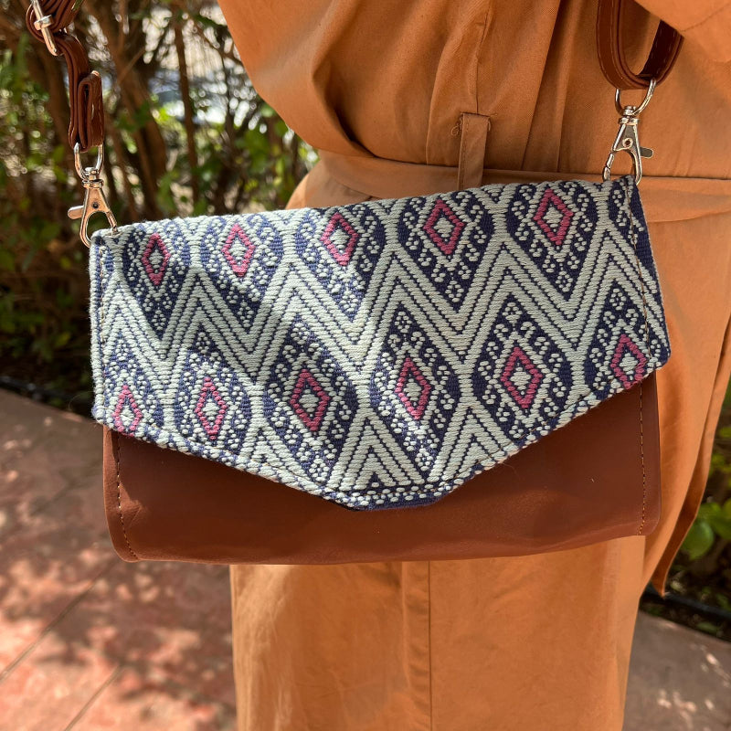 Woman wearing a brown leather crossbody bag with black and grey geometric woven flap outdoors