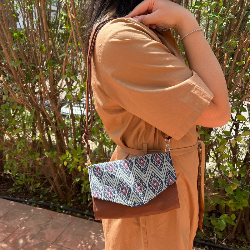 Woman wearing a brown leather crossbody bag with black and grey geometric woven flap outdoors