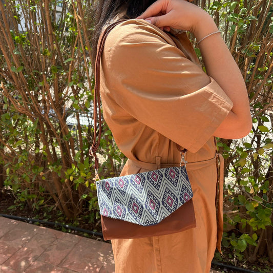 Woman wearing a brown leather crossbody bag with black and grey geometric woven flap outdoors