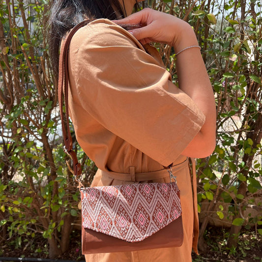 Woman wearing a brown leather crossbody bag with rose pink geometric woven flap outdoors