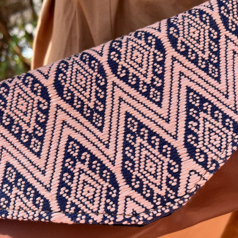 Woman wearing a brown leather crossbody bag with beige and navy geometric woven flap outdoors
