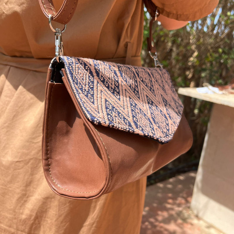 Woman wearing a brown leather crossbody bag with beige and navy geometric woven flap outdoors