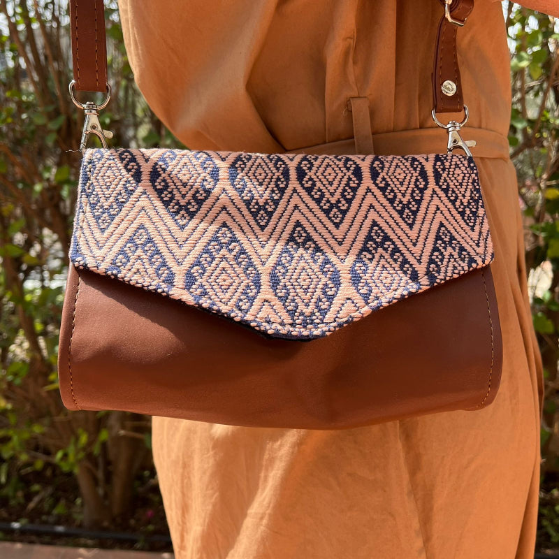 Woman wearing a brown leather crossbody bag with beige and navy geometric woven flap outdoors